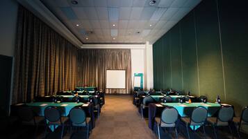 Una sala conferenze con diversi tavoli e sedie, uno schermo per proiettore e una parete verde.