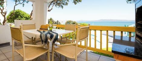 A covered patio with a table and chairs, overlooking a scenic view of the sea.