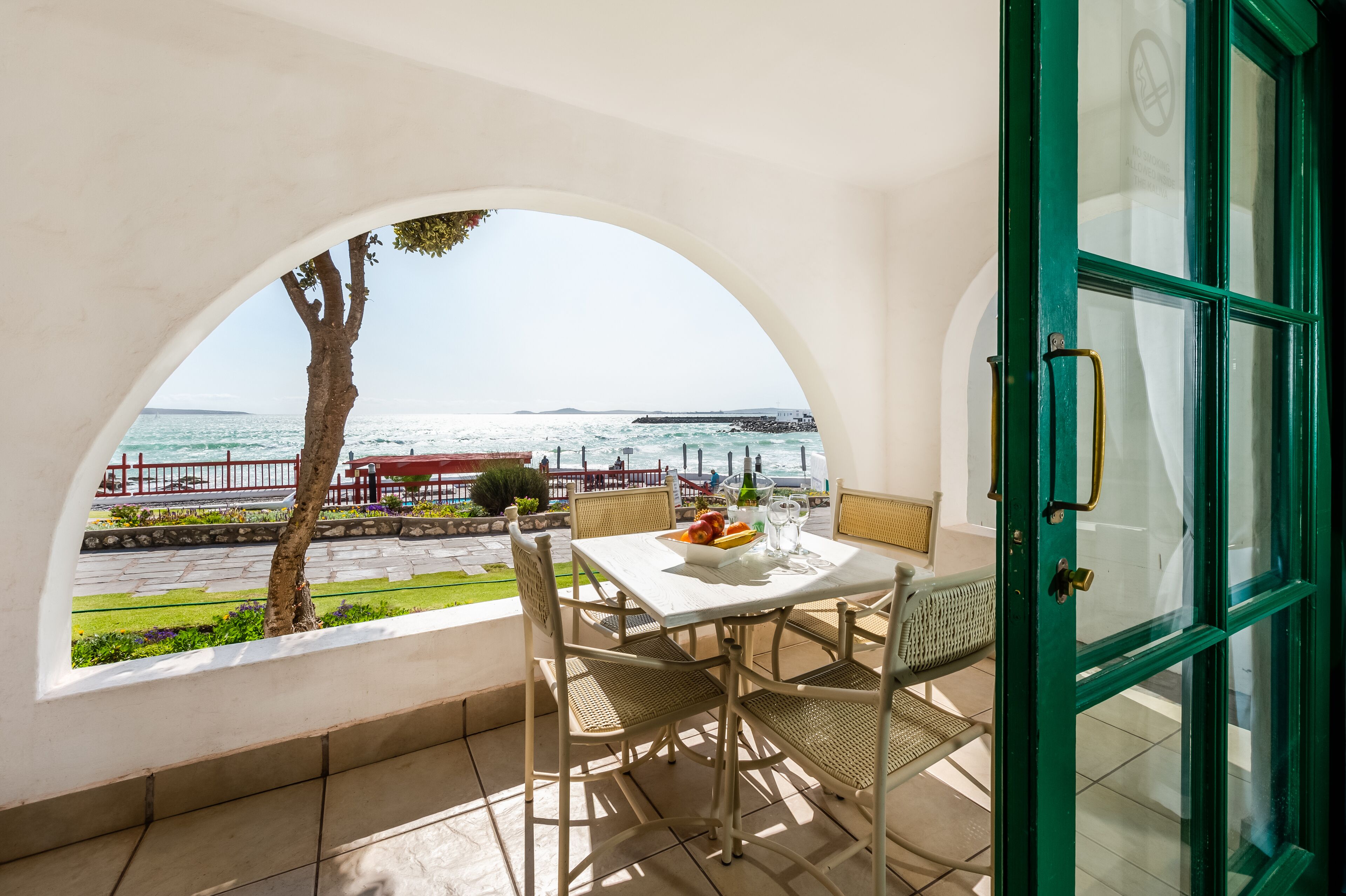 Un balcón con mesa y sillas, con vista a una zona costera y al mar, incluyendo un muelle.