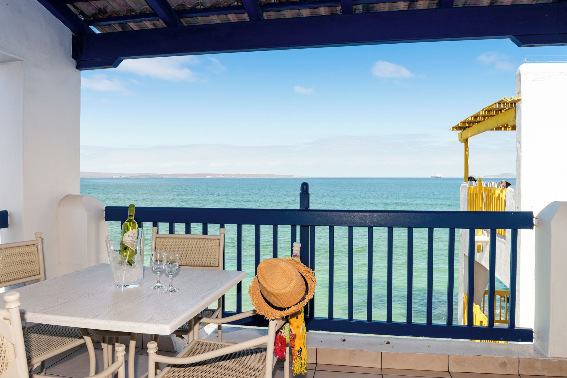 A balcony with a table, chairs, a bottle of wine, and a straw hat.