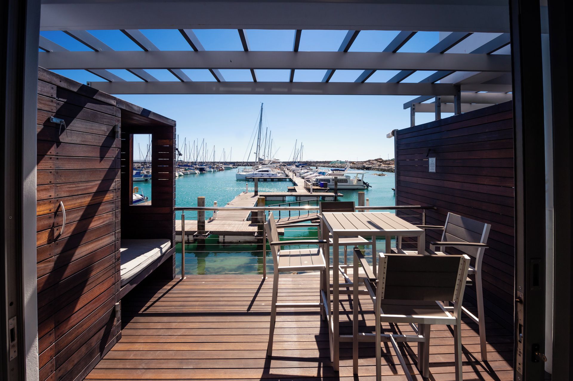 A wooden deck with a view of a marina, outdoor seating, and a pergola structure.