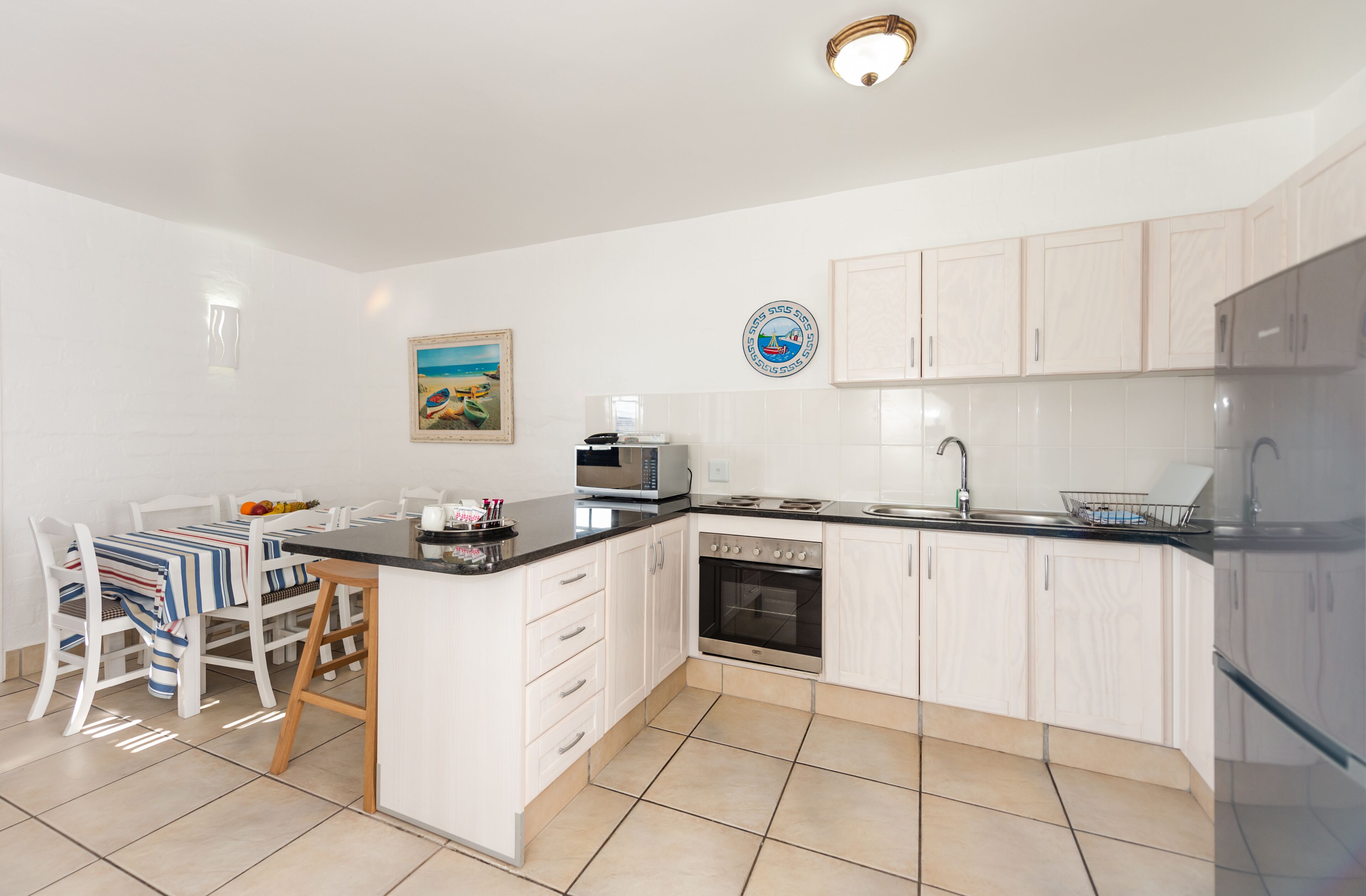 A modern kitchen with white cabinets, a microwave, an oven, and a sink. There is a dining area with a table and chairs.