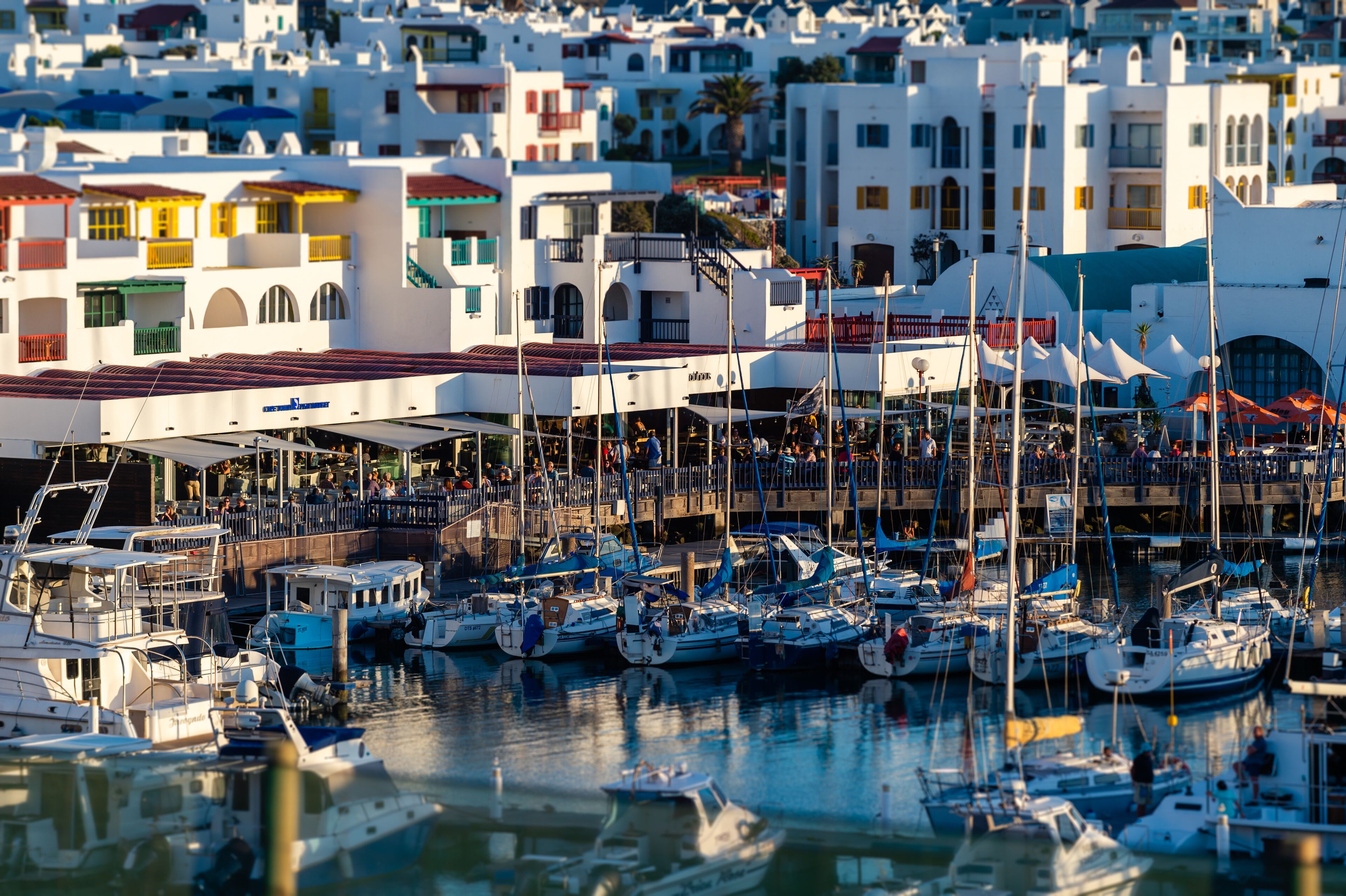 A marina with numerous boats docked, surrounded by white buildings with balconies and red roofs.