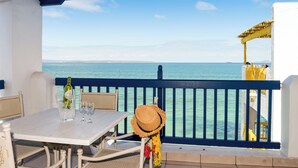 Un balcone con tavolo, sedie, una bottiglia di vino e un cappello di paglia.