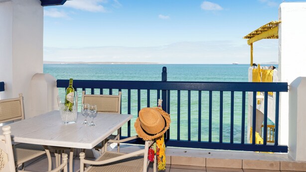 A balcony with a table, chairs, a bottle of wine, and a straw hat. - Club Mykonos Langebaan (Langebaan)