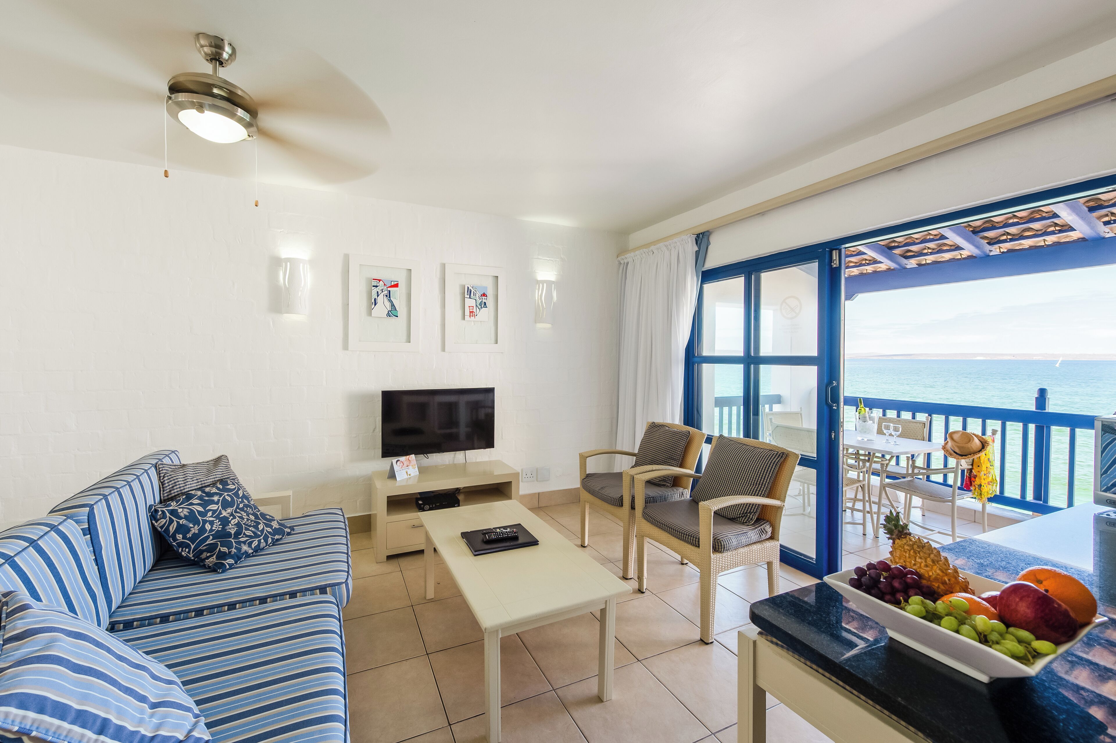Una sala de estar con sofá, mesa de centro, televisor y un balcón con vista al mar.