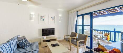 Una sala de estar con sofá, mesa de centro, televisor y un balcón con vista al mar.