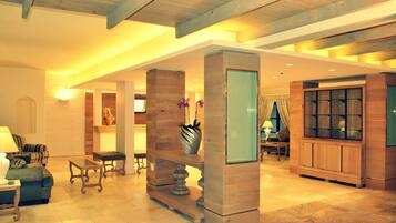 A spacious lobby with a high ceiling, wooden beams, a reception desk, seating area, and a large mirror.