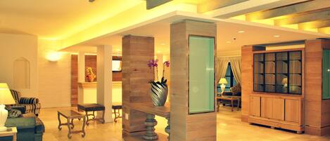 A spacious lobby with a high ceiling, wooden beams, a reception desk, seating area, and a large mirror.