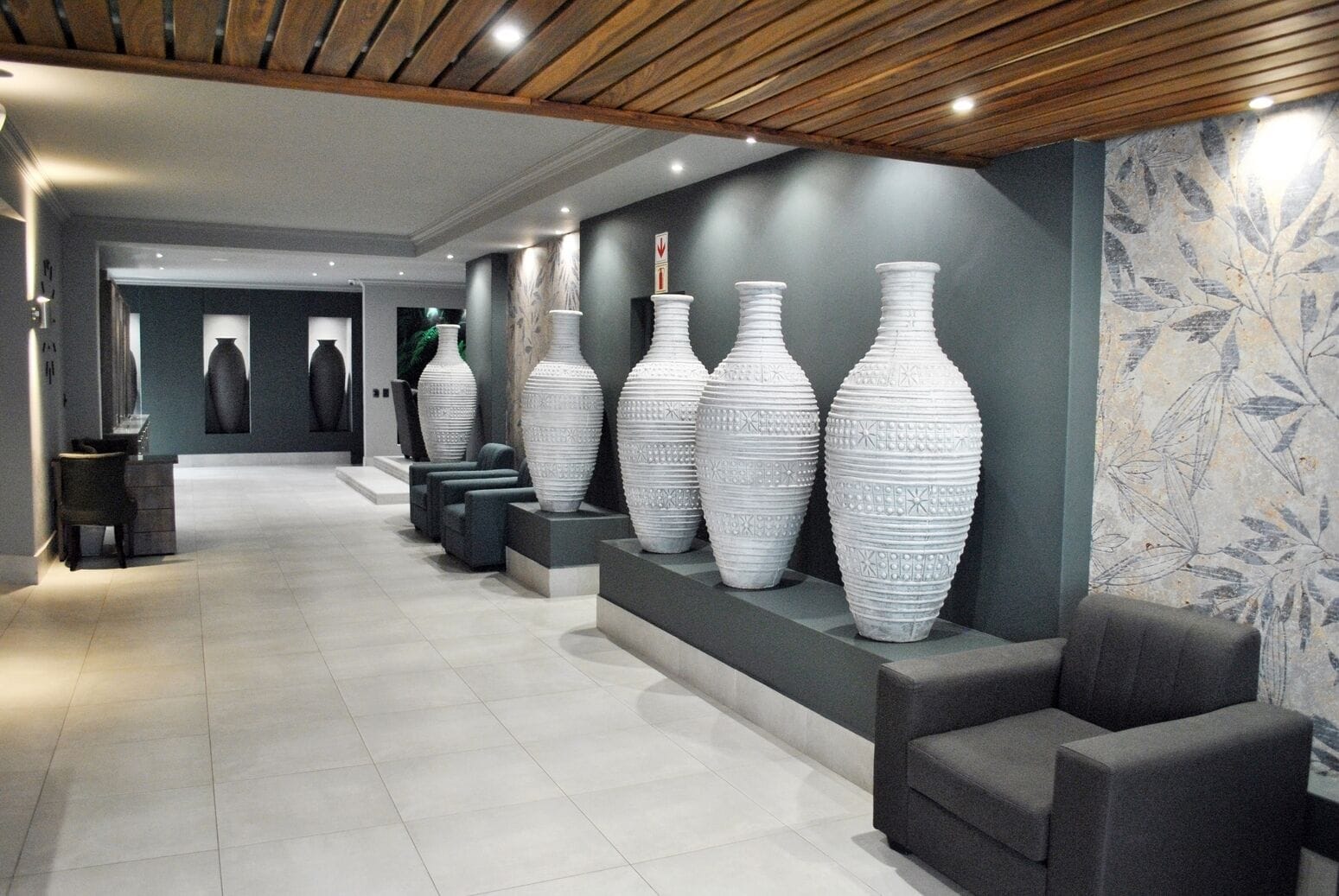 A modern lobby with a long corridor, large white vases on display, and a seating area with grey sofas.