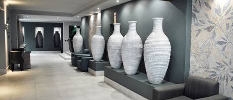 A modern lobby with a long corridor, large white vases on display, and a seating area with grey sofas.