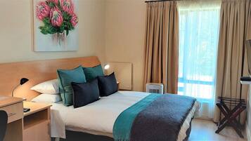 A hotel room with a bed, a desk with a lamp, a TV, and a painting on the wall.