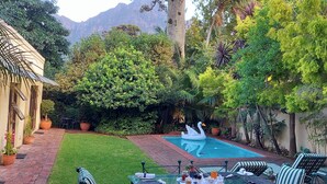 A backyard with a swimming pool, a swan float, and a patio area with chairs and tables. - Riversong Guest House (Cape Town)