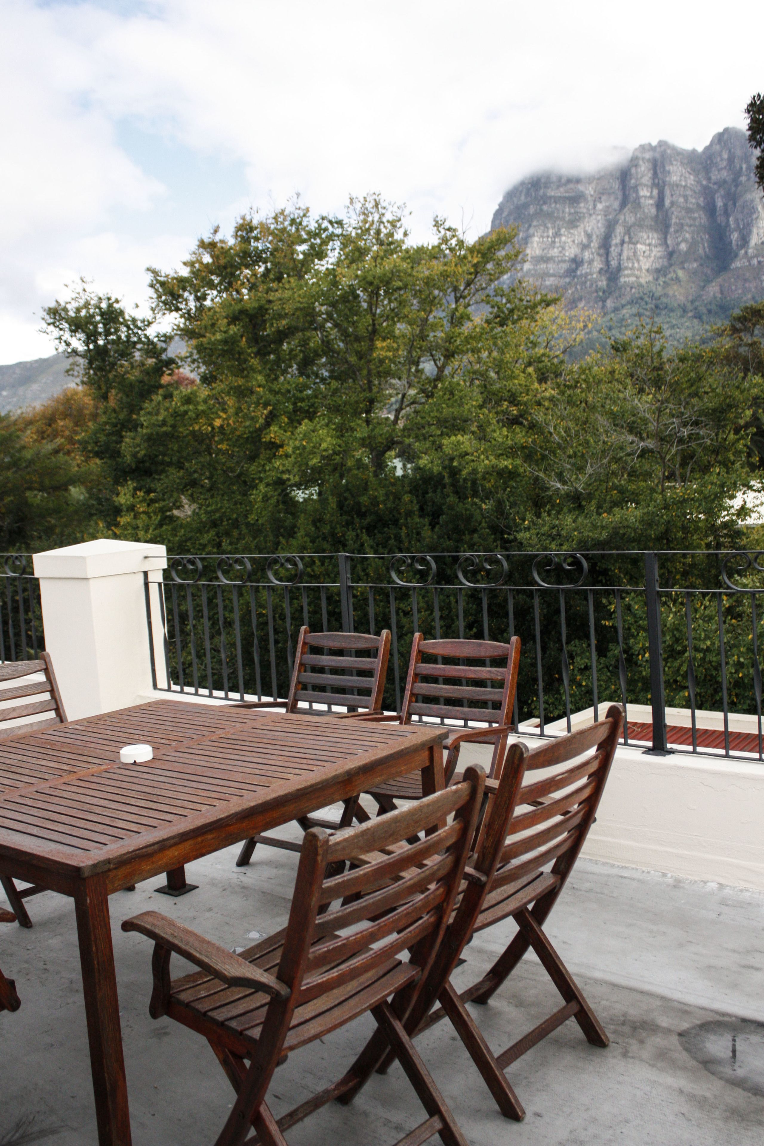 Una mesa y sillas de madera en una terraza exterior con vista a una cadena montañosa.