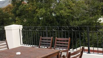 Una mesa y sillas de madera en una terraza exterior con vista a una cadena montañosa.