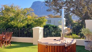 An outdoor patio with a hot tub, wooden chairs, and a view of a mountain. - Riversong Guest House (Cape Town)