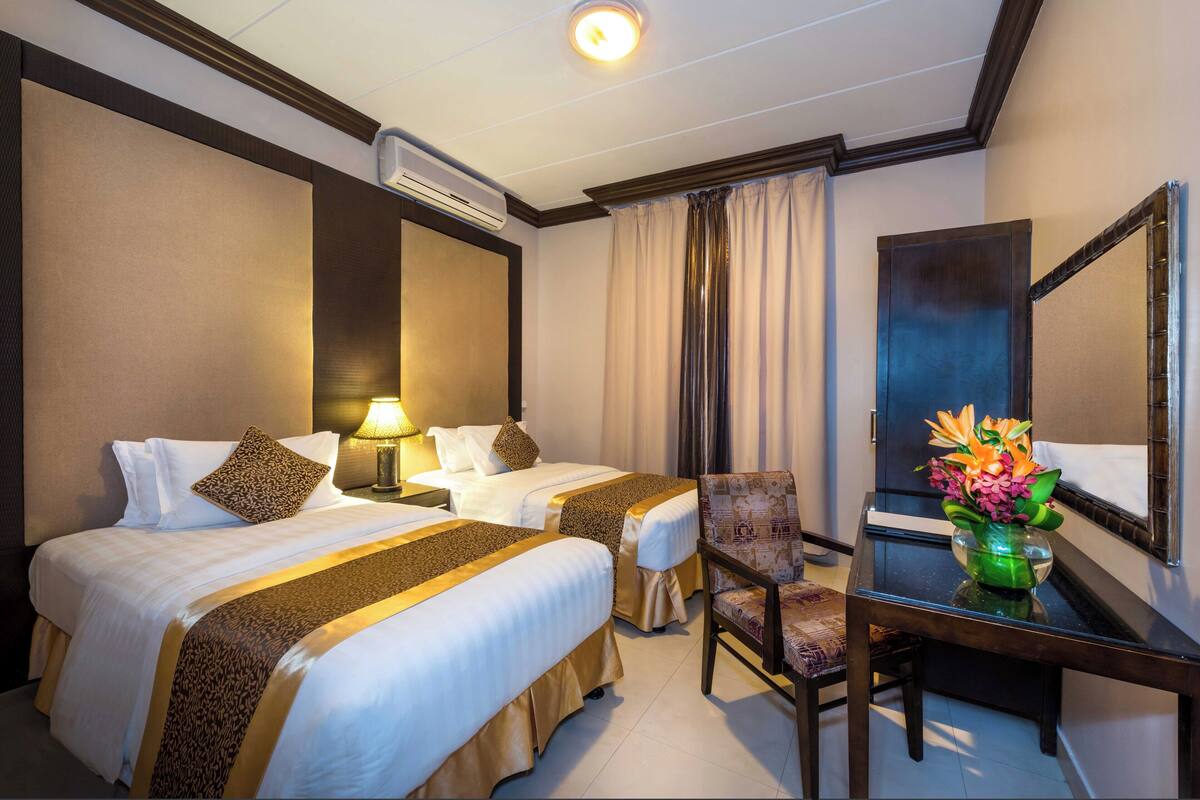 A hotel room with two beds, a desk, a chair, and a mirror.