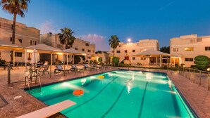 A swimming pool with lounge chairs and umbrellas, surrounded by buildings with balconies and palm trees. - Boudl Al Malaz (Riyadh)