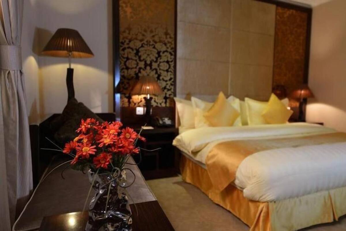 A hotel room with a bed, a nightstand, a lamp, and a vase with flowers.