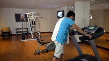 A gym with a treadmill, weight machines, and a TV screen.