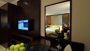 Hotellihuone, jossa on televisio, valkoisilla lakanoilla varustettu sänky, peili sekä pöytä, jonka pä ällä on kulho vihreitä omenoita ja kirja.