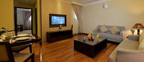 Una sala de estar con televisor, un sofá, una mesa de centro y un comedor con mesa lista para dos.