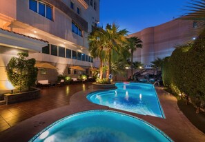 A hotel pool area with a curved pool, palm trees, and outdoor seating. - Boudl Al Shatea (Dammam)