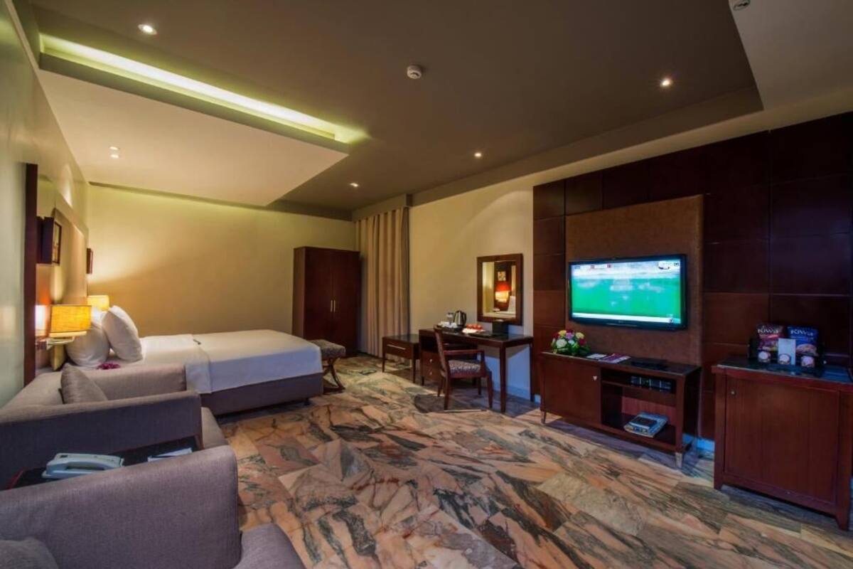 A hotel room with a bed, a desk, a television, and a seating area.