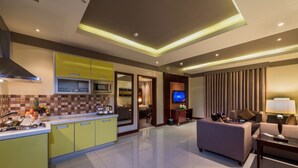 Una habitación de hotel moderna con cocina, sala de estar con sofá y televisor, y comedor.