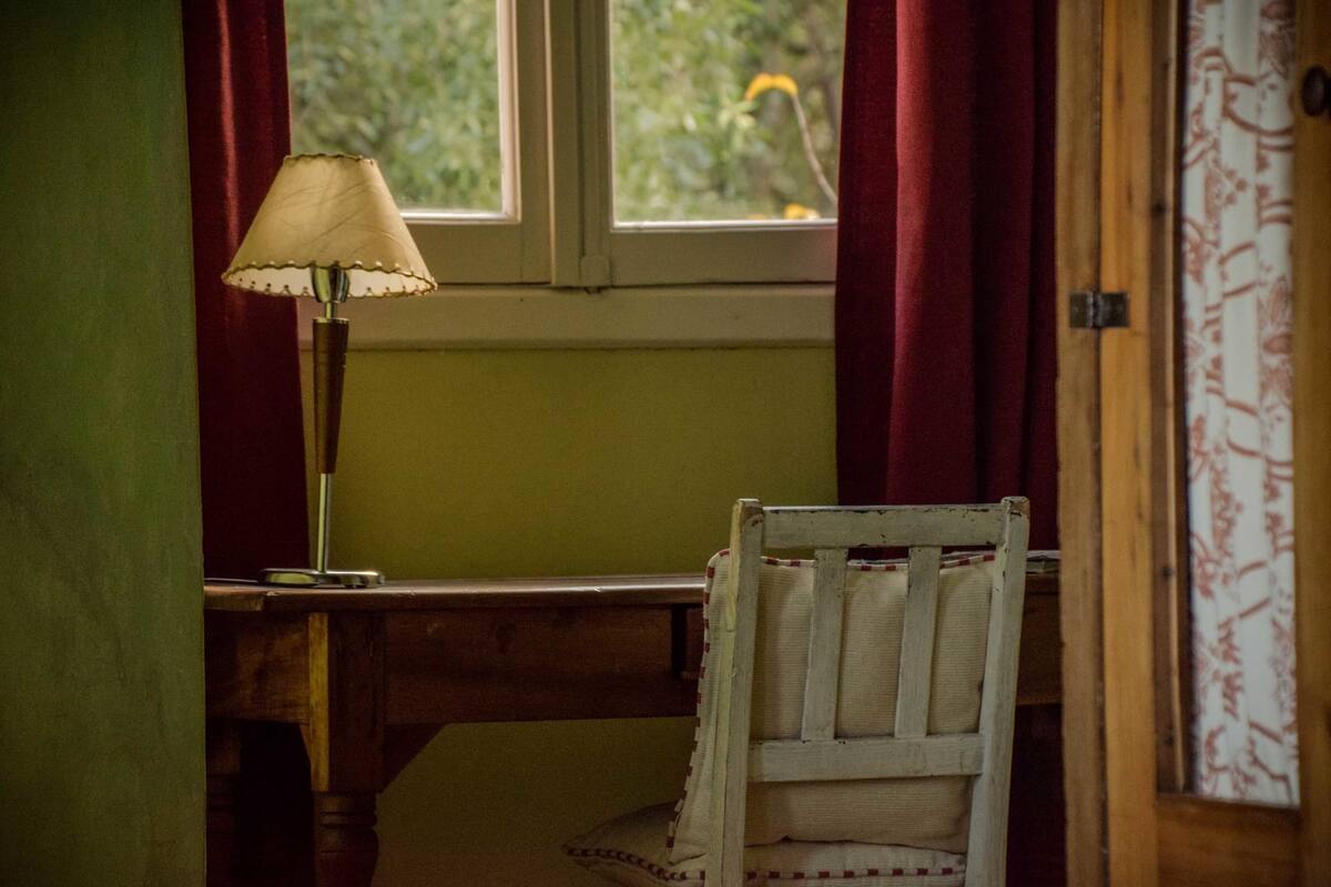 A room with a wooden desk, a chair, a lamp, and a window with curtains.