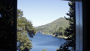 A lake surrounded by dense forest and hills, viewed through a window with a wooden frame. - Los Juncos Patagonian Lake House (San Carlos de Bariloche)