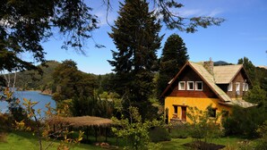 A yellow house with a sloped roof, surrounded by a lush green landscape and a lake. - Los Juncos Patagonian Lake House (San Carlos de Bariloche)