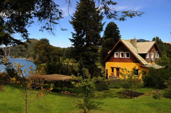 Une maison jaune, dotée d’un toit en pente, entourée d’un paysage verdoyant et luxuriant et bordée d’un lac.