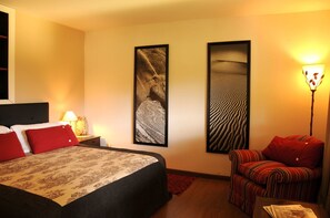 Une chambre d’hôtel avec un lit, une table de chevet, une lampe, deux tableaux encadrés au mur et une chaise à rayures.