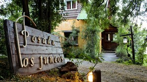 A wooden sign with the text "Posada los Juncos" in a rustic style, leading to a wooden house surrounded by trees. - Los Juncos Patagonian Lake House (San Carlos de Bariloche)