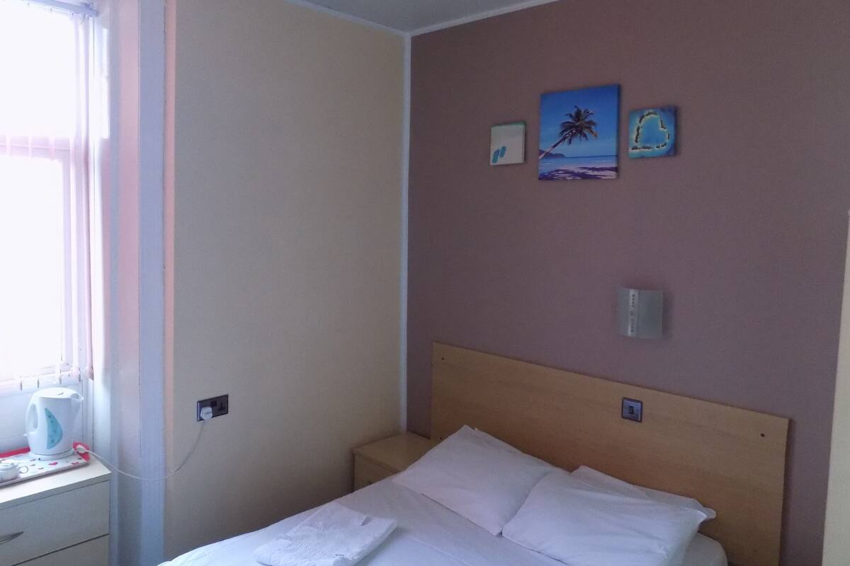 Una habitación de hotel con cama, mesita de noche, ventana con cortinas y decoración en la pared.