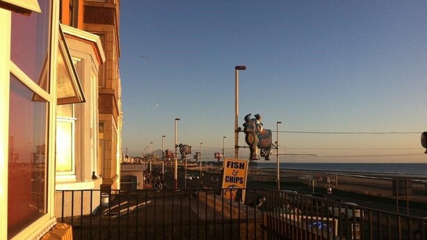 A coastal view with a sign for 'Fish & Chips' restaurant, a metal fence, and a clear sky. - The New Royal Windsor Hotel (Blackpool)