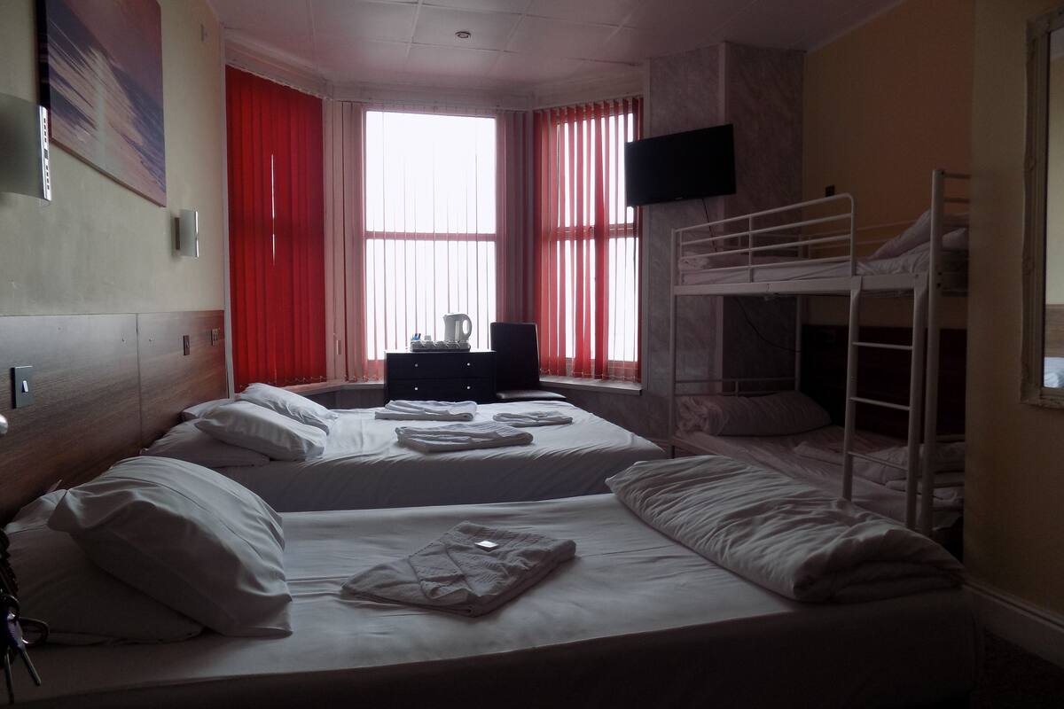Habitación de hotel con dos camas, televisión, escritorio y ventana con cortinas.