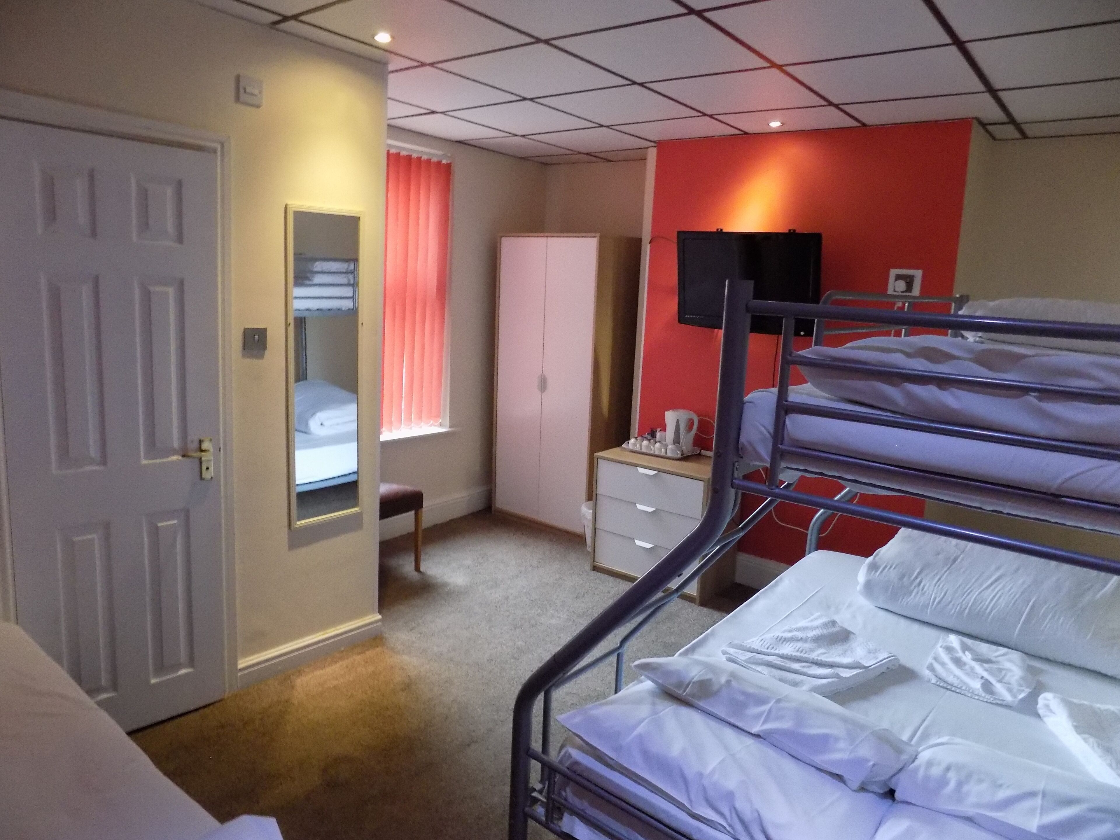 A bedroom with bunk beds, a wardrobe, a bedside table with a lamp, and a window with curtains.