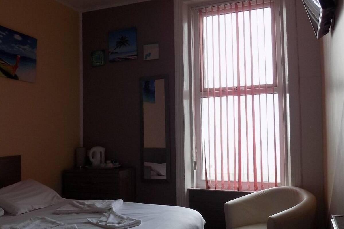 Una habitación de hotel con cama, una silla, cómoda y ventana con persianas.