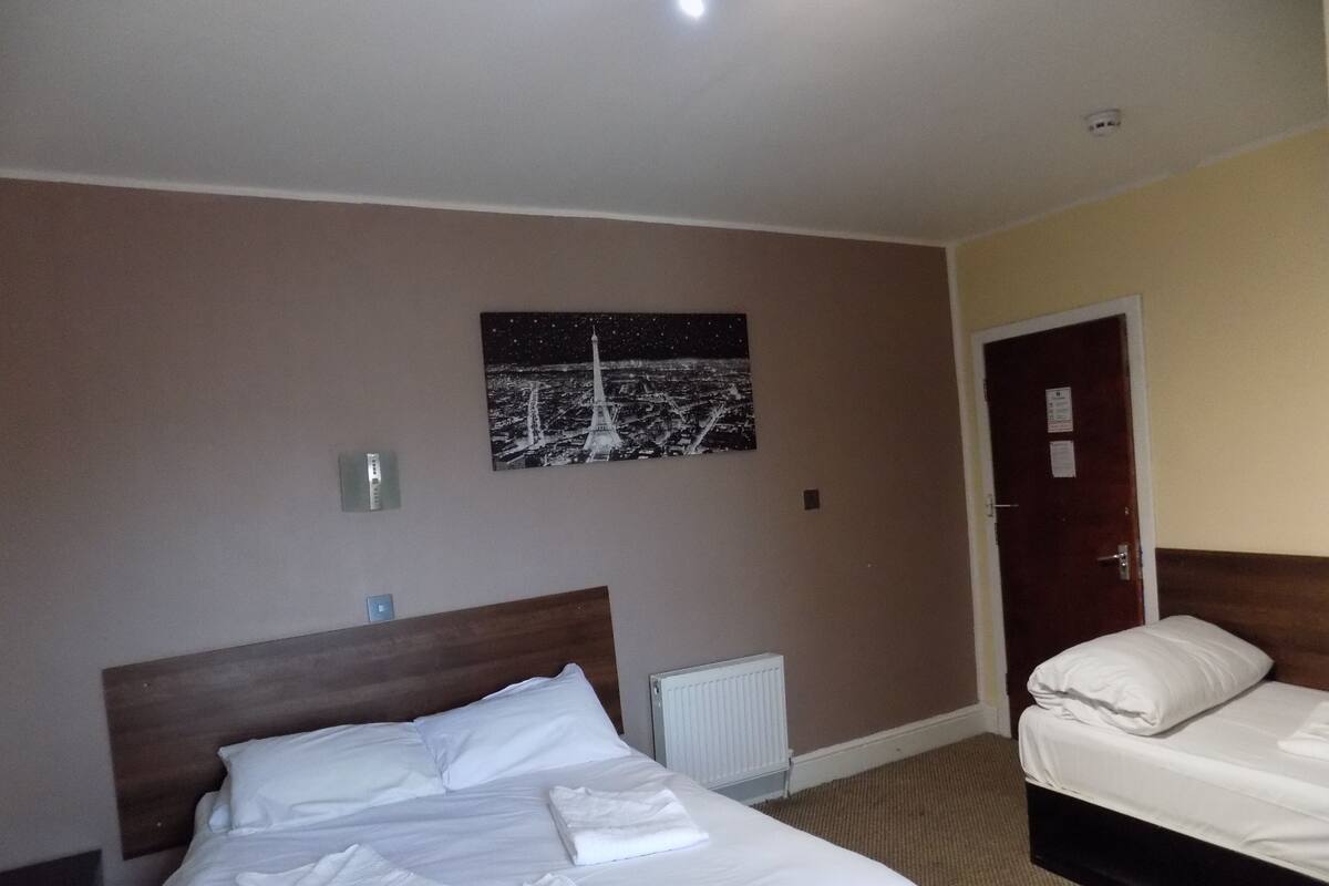 Una habitación de hotel con una cama grande, una cama más pequeña, una imagen del cielo nocturno en la pared y una puerta a la derecha.