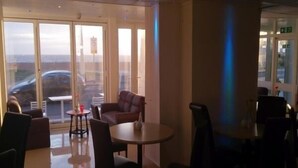 A modern interior with a seating area featuring a round table and chairs, large windows with a view of the city, and a glass door leading outside. - The New Royal Windsor Hotel (Blackpool)