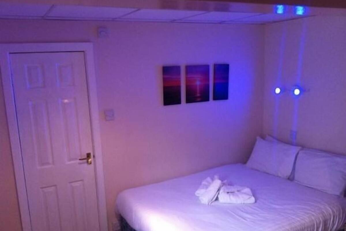 Un dormitorio con cama, ropa de cama blanca, una puerta y apliques.