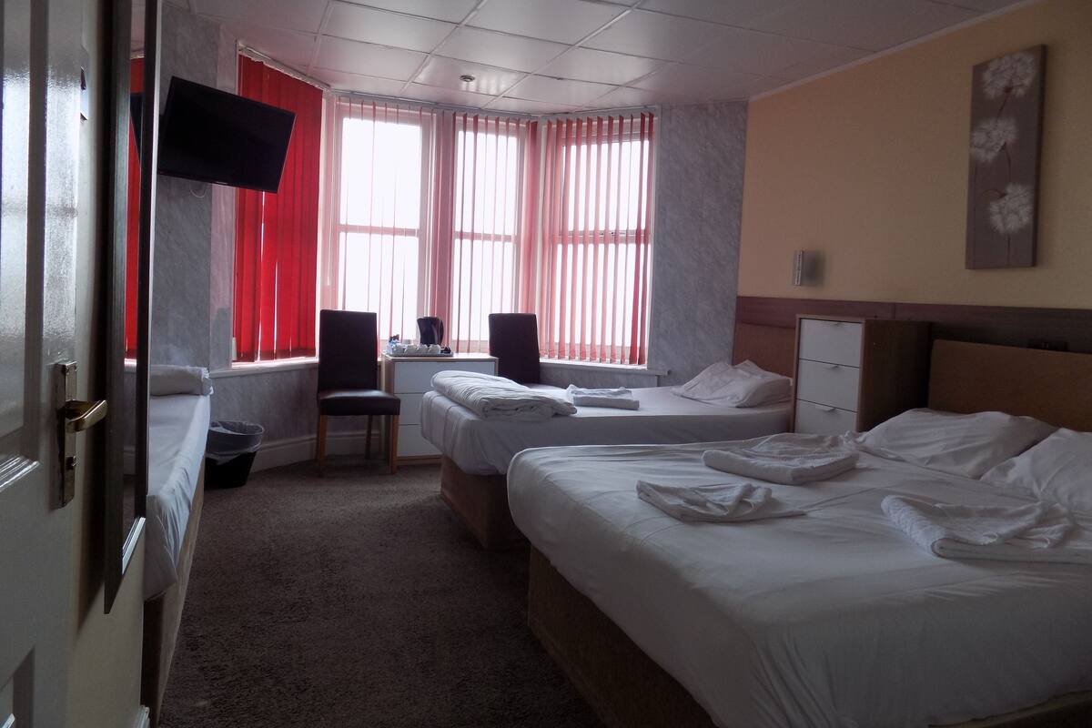 Una habitación de hotel con dos camas, un escritorio, una silla, un televisor y una ventana con cortinas.