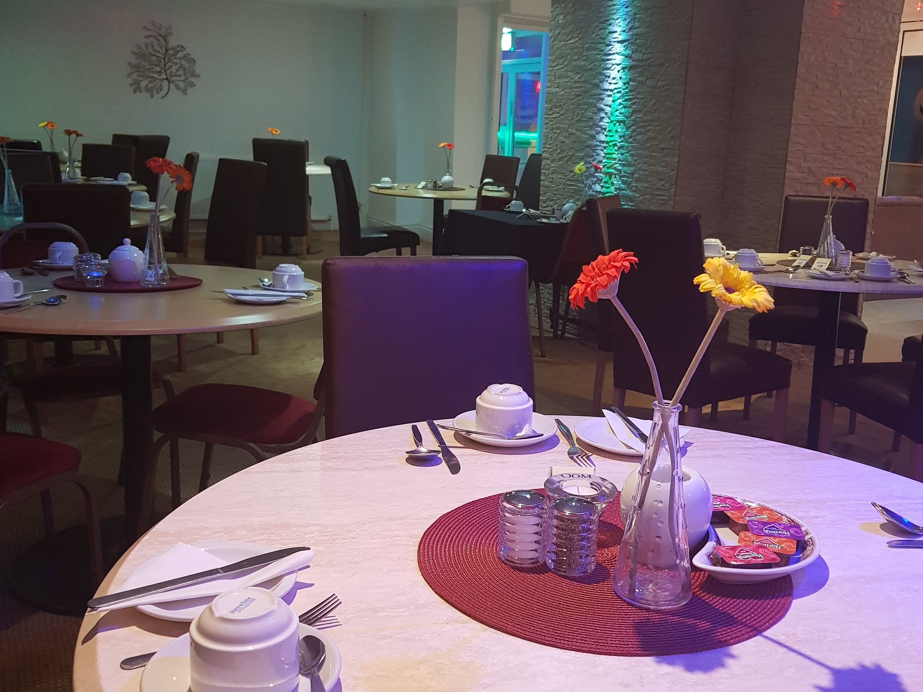 A dining area with round tables, chairs, and a variety of table settings including plates, cutlery, and decorative items.