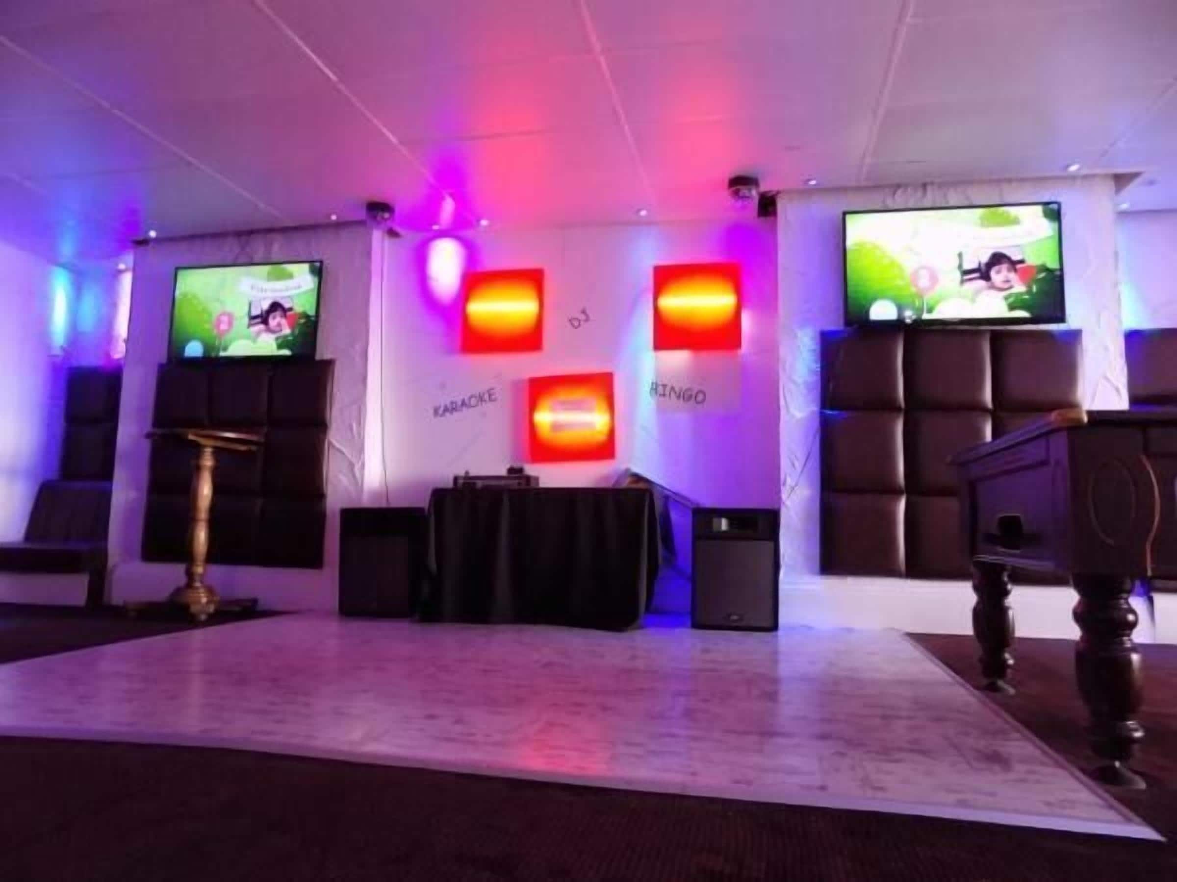 Een kamer met een podium, karaoke-installatie en grote schermen waarop een cartoonfiguur wordt getoond.