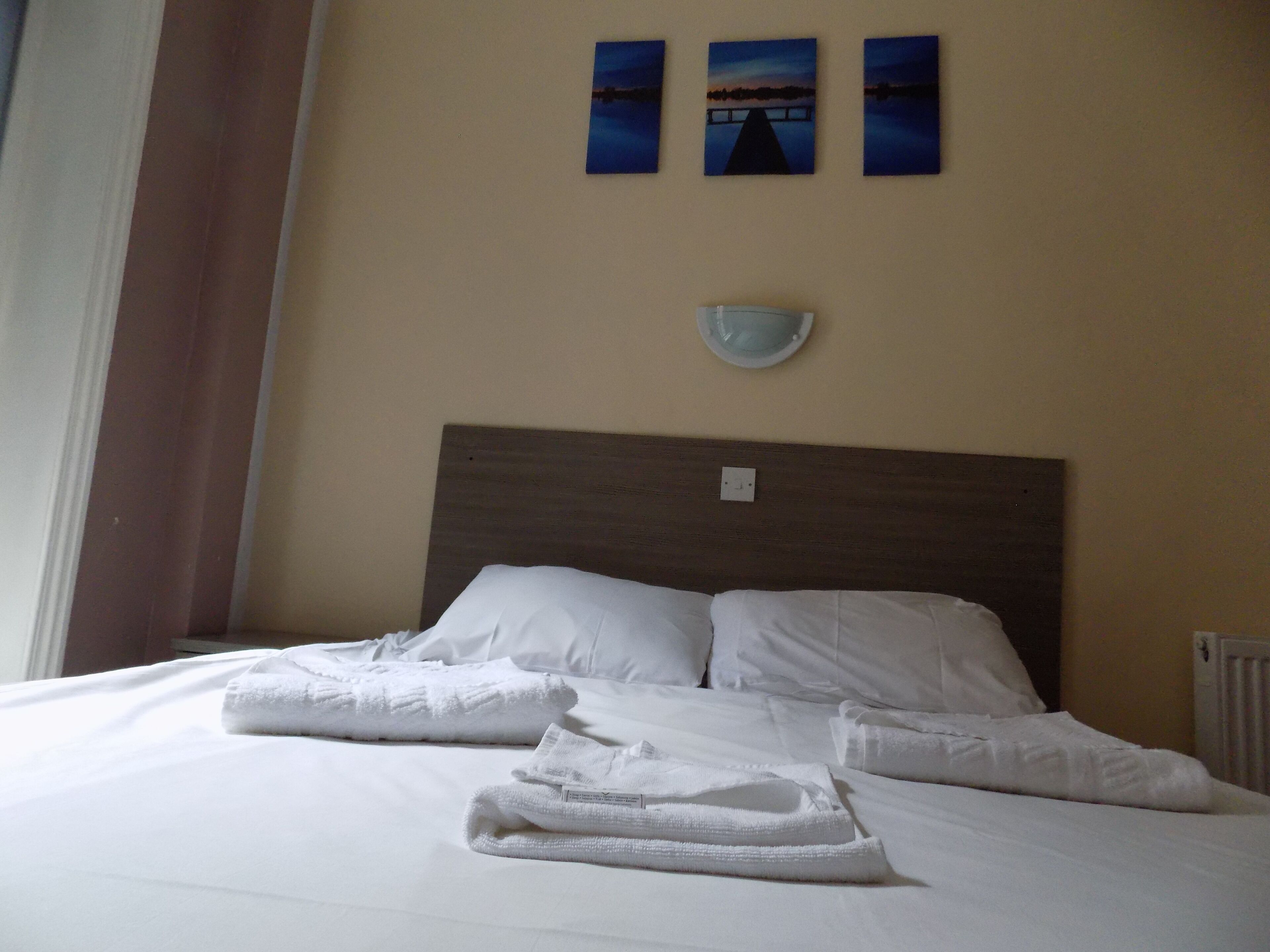 A neatly made bed with white linens and towels, a wooden headboard, and three framed pictures on the wall.