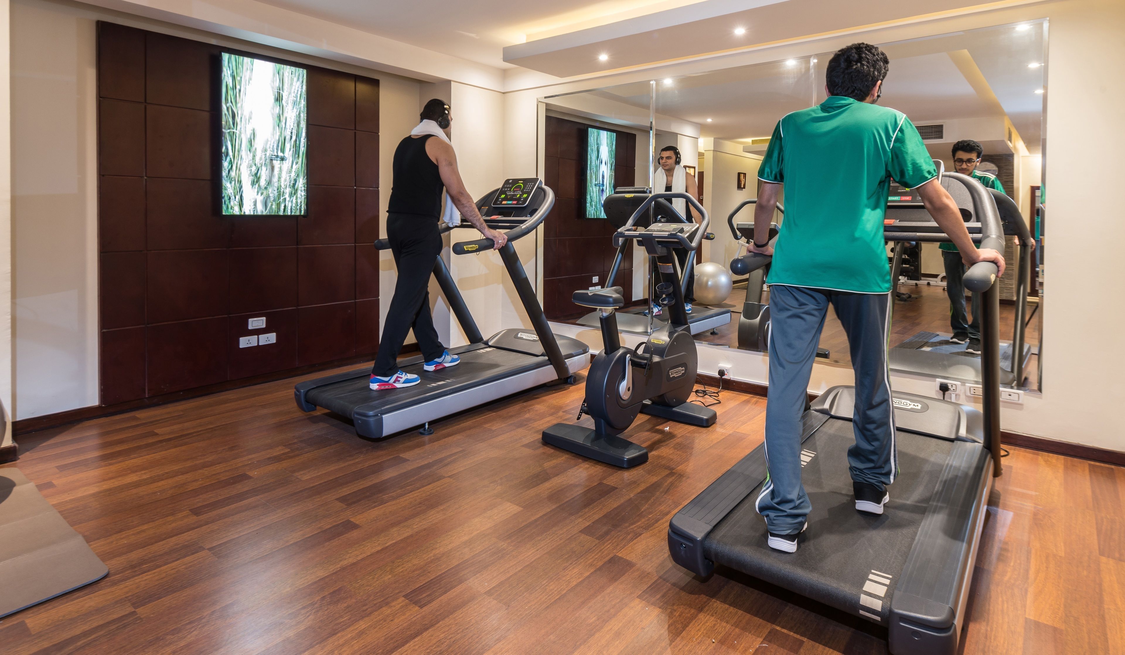 Une salle de sport équipée de tapis de course, de vélos d’exercice et d’un mur recouvert de miroirs.
