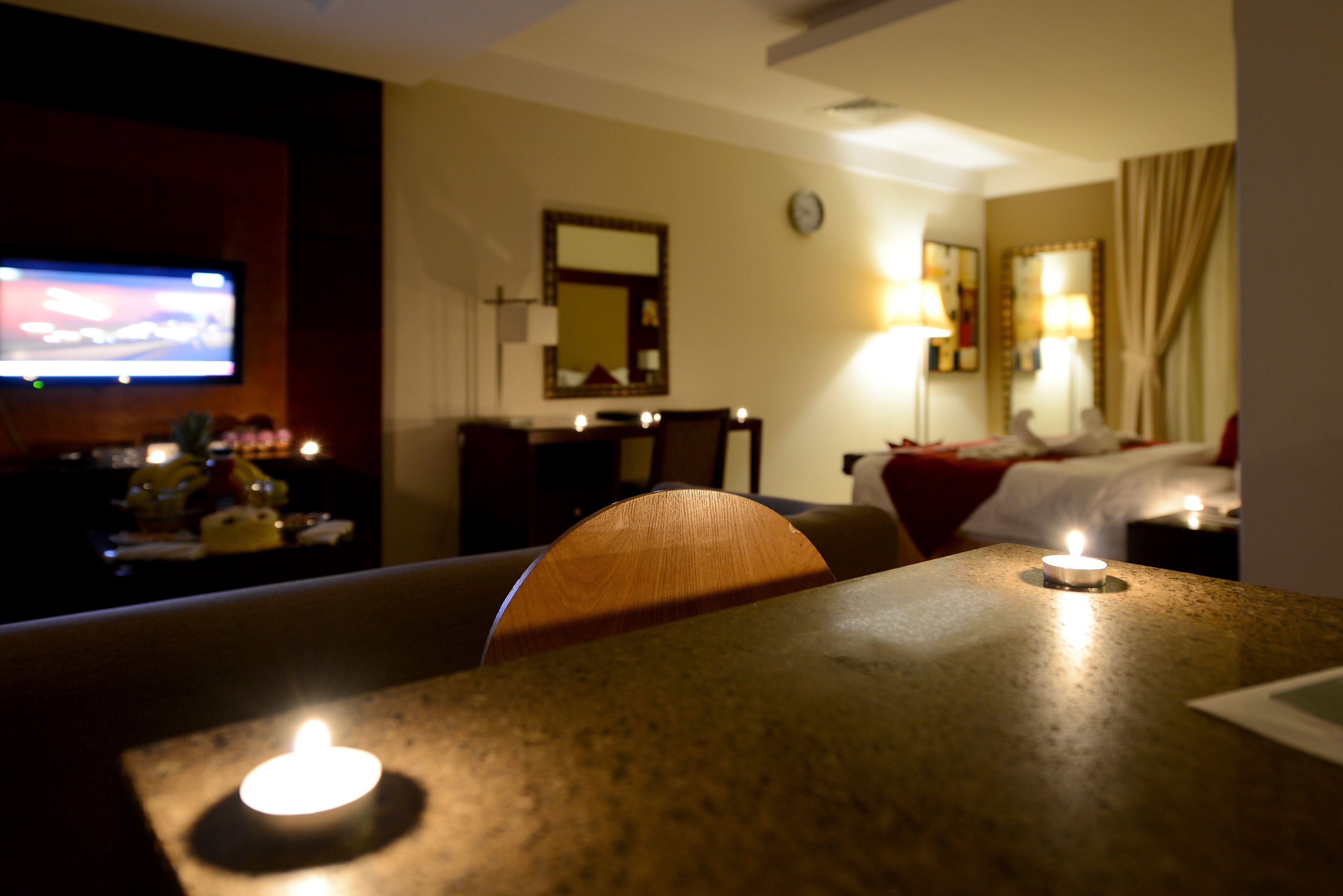 Habitación de hotel con televisión, cama, escritorio con vela y espejo en la pared.