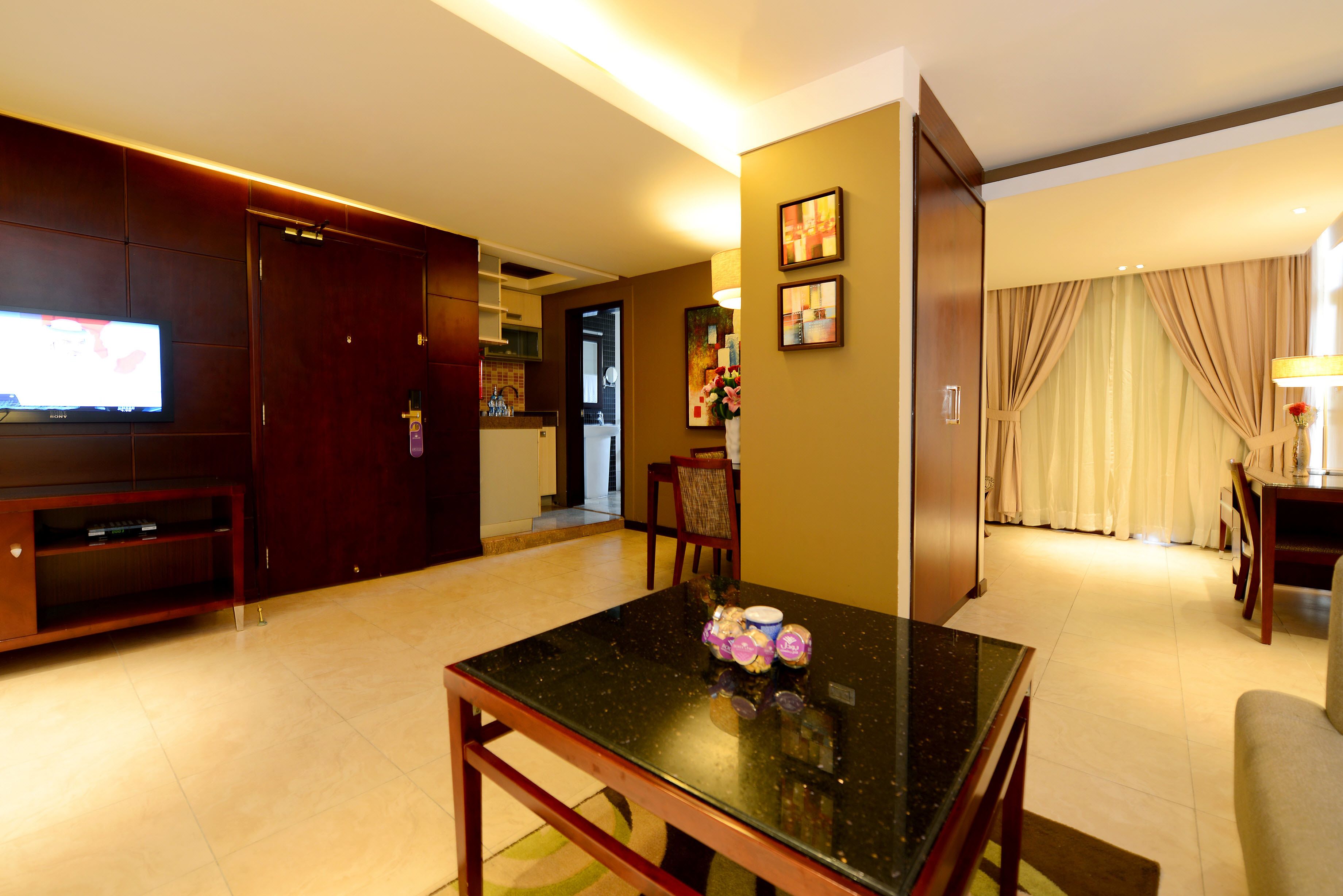 A hotel room with a dining table, a TV, and a living area with a sofa and curtains.